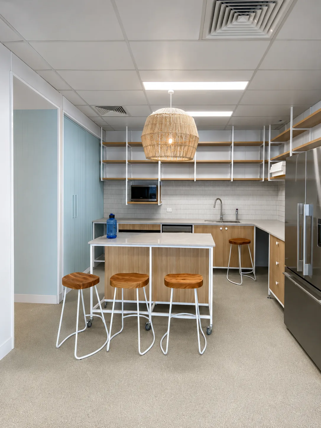 Compact commercial kitchenette with pale blue cabinetry, white subway tiles and timber accents, painted by Paint Gods.