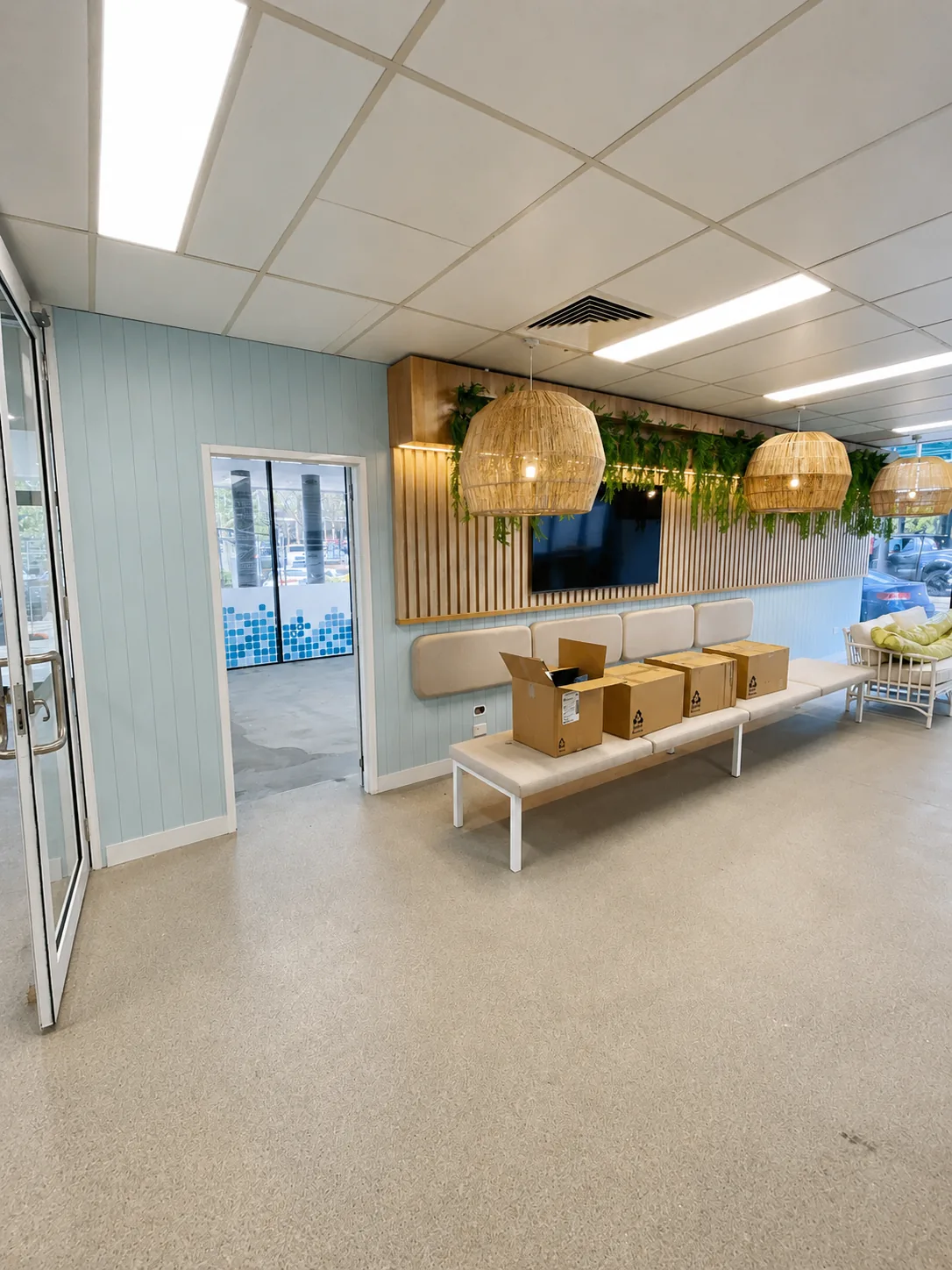 Commercial reception and waiting area with pale blue walls, a timber-slat feature wall with greenery and terrazzo flooring, painted by Paint Gods.