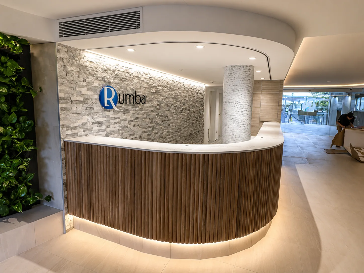 Curved timber-slat reception desk at Rumba Resort with a stone feature wall, greenery and warm lighting, finished by Paint Gods.
