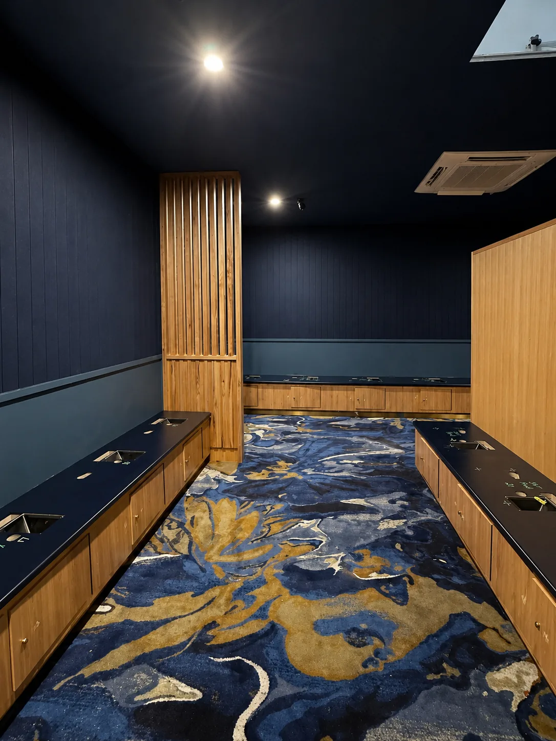 Dark navy media room with timber-slat walls, blue and gold patterned carpet and moody downlighting, painted by Paint Gods.