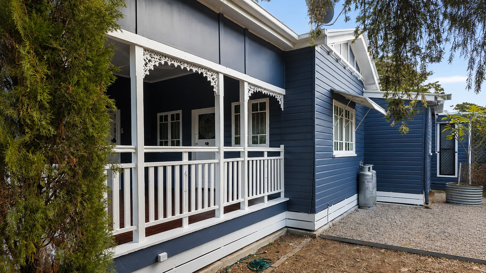 Blue weatherboard Queenslander home with a white timber verandah, decorative lace brackets and crisp white trims, painted by Paint Gods.