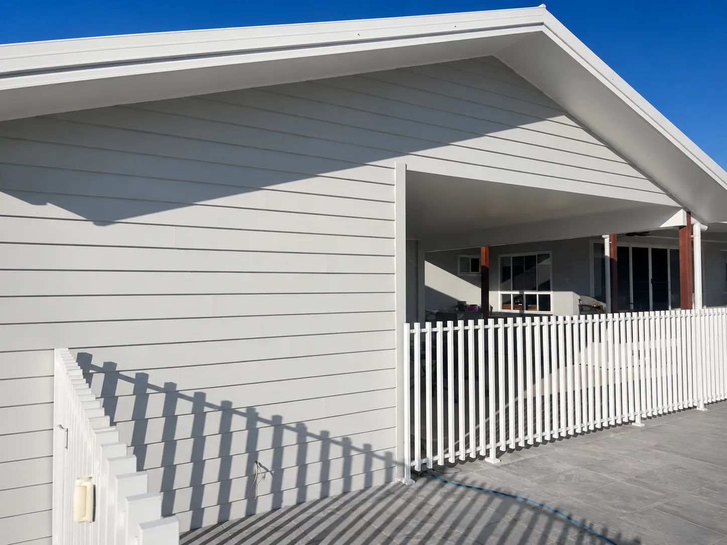 Freshly painted light-grey weatherboard home with a gable end and white picket fence under a clear blue sky.
