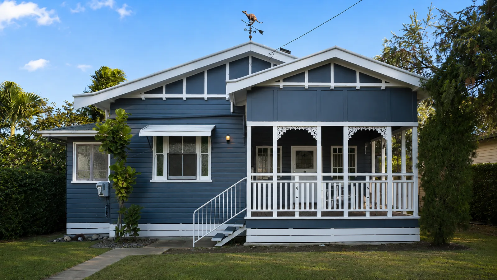 After, the same Queenslander home repainted by Paint Gods in a deep blue-grey with crisp white trims, gables and verandah detailing.