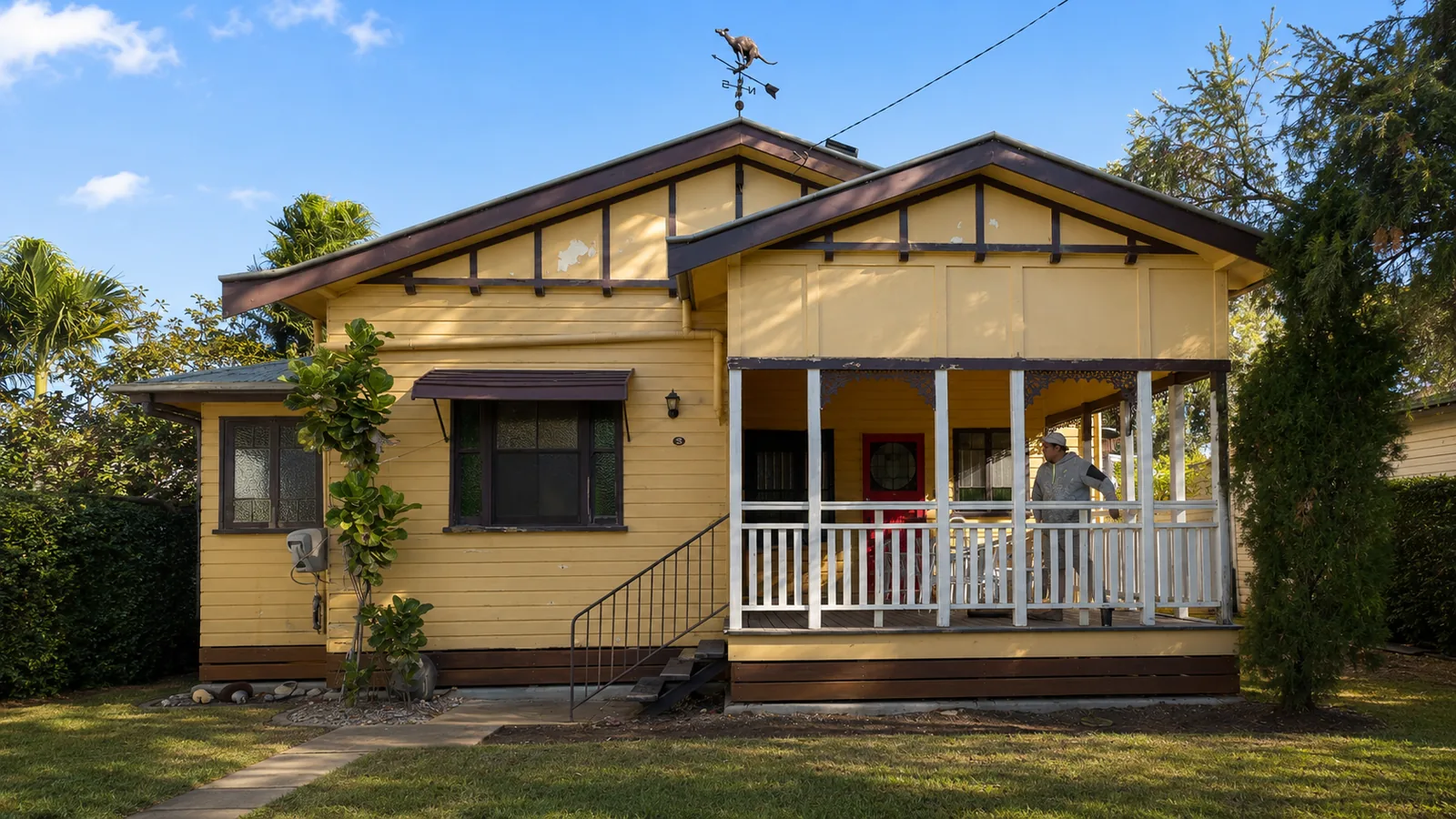Before, a tired weatherboard Queenslander home with faded yellow paint and dark brown trims, ready for a full exterior repaint by Paint Gods.
