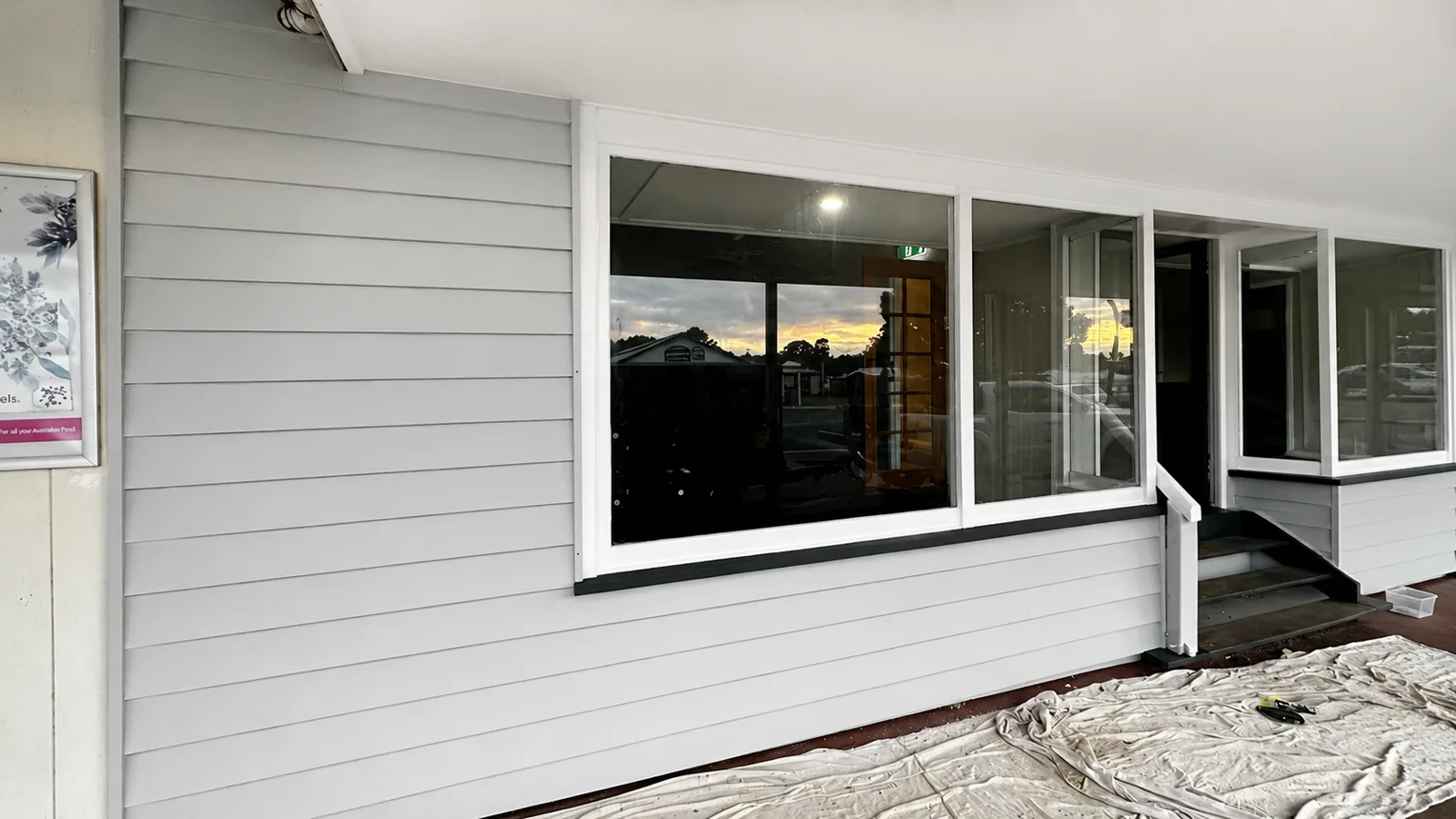 After, the same commercial shopfront repainted by Paint Gods in fresh light-grey weatherboards with crisp white window trims.