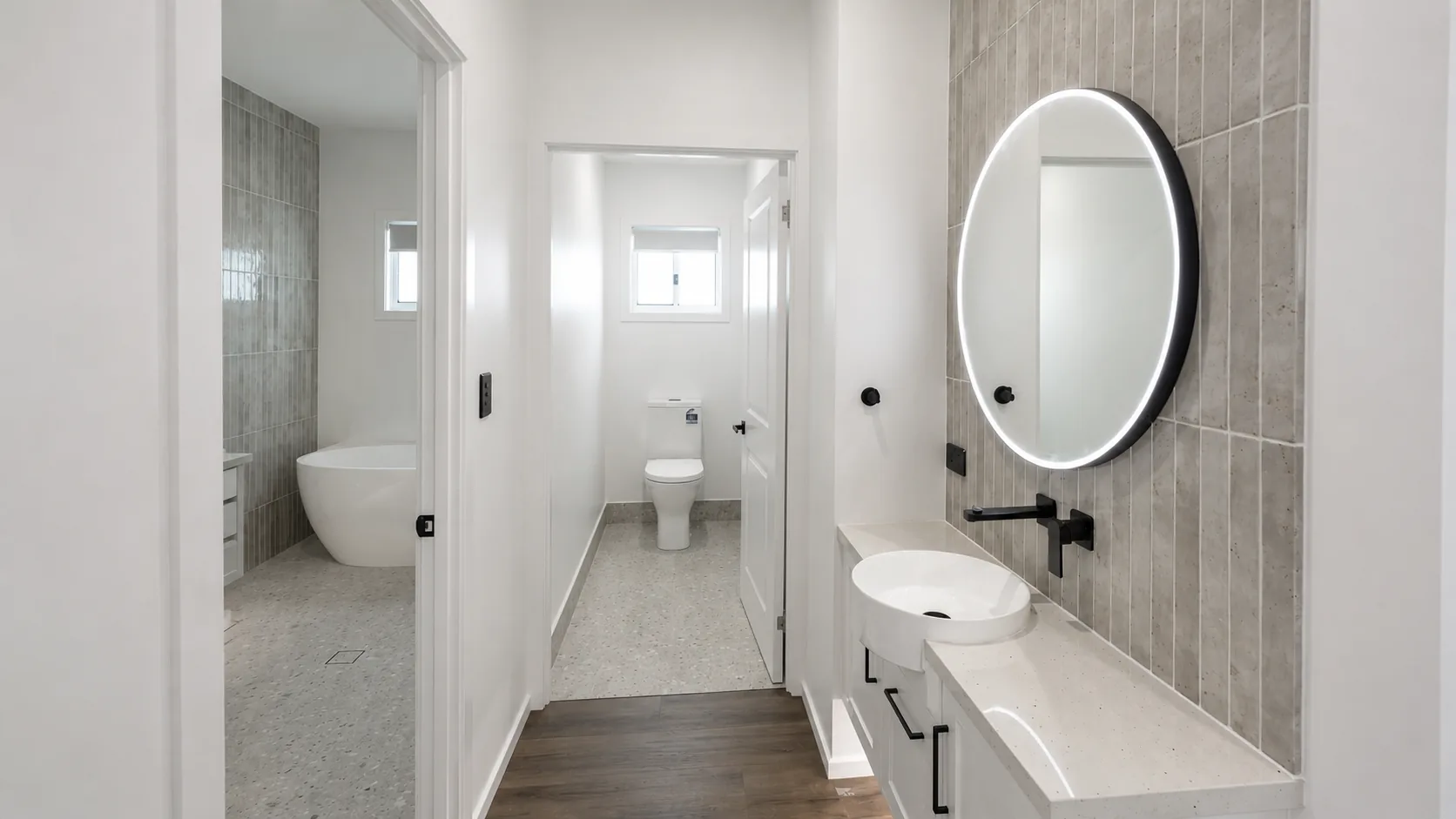 Bright modern ensuite with crisp white walls, a freestanding bath, tiled feature wall and timber-look floor, painted by Paint Gods.